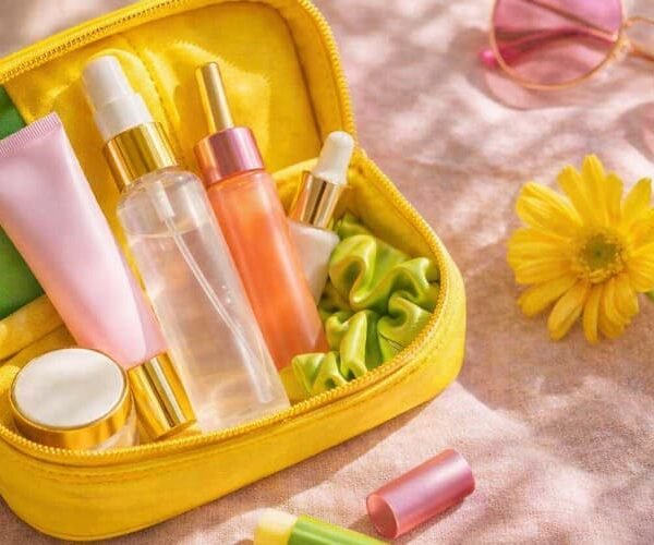 Luxury summer travel beauty flat-lay with skincare essentials in an open cosmetic pouch, including sunscreen, face mist, lip balm and sunglasses in warm natural sunlight