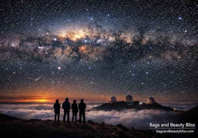 Four people stargazing at Mauna Kea , Hawaii, under the Milky Way with observatory domes above the clouds