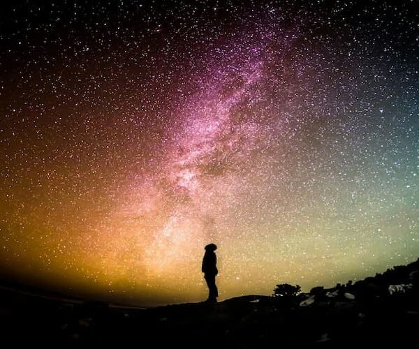 Silhouette of a person standing beneath the Milky Way galaxy under a colorful star‑filled night sky