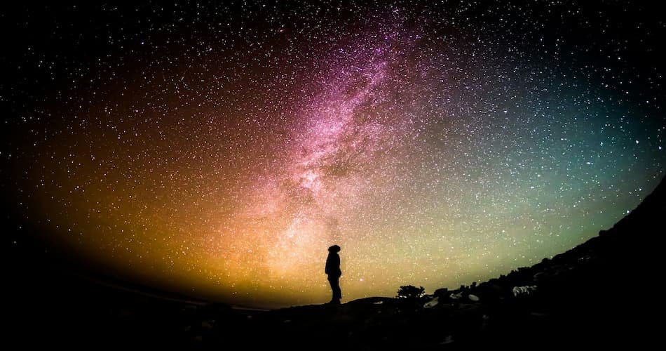 Silhouette of a person standing beneath the Milky Way galaxy under a colorful star‑filled night sky