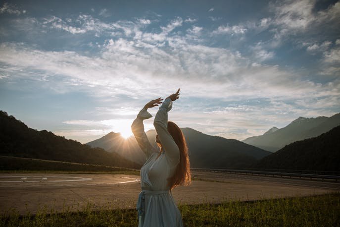 Woman in a pastel shade dress feeling reconnected with herself at a Bali sunrise behind the mountains.