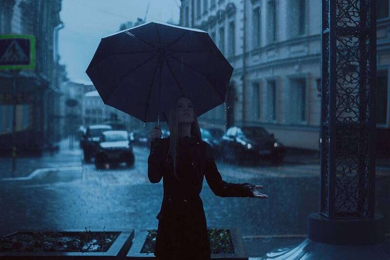 Traveler with umbrella walking through a rainy street during Halloween ghost walk in the USA.