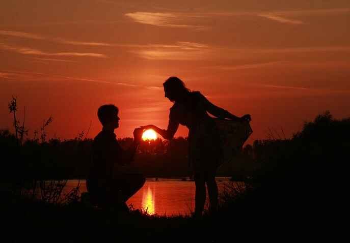 Romantic silhouette of a couple holding hands at sunset by the water with sun’s glow in it.