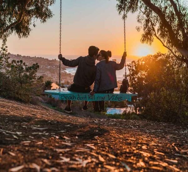 Couple sitting on a swing overlooking a scenic coastal view at sunset