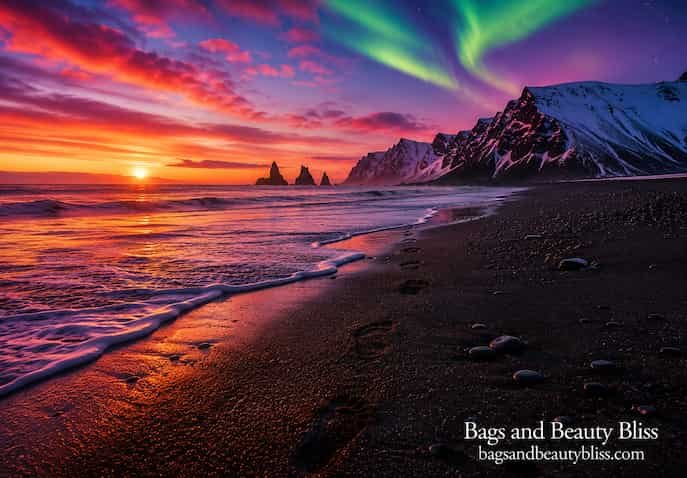  Human footprints leading toward the ocean on a black sand beach in Iceland beneath colorful sunset skies, Northern Lights, and dramatic snow-covered mountains.