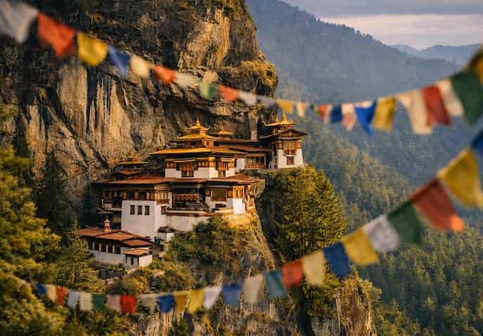  Tiger’s Nest Monastery perched on a cliff in Bhutan’s Paro Valley, surrounded by pine forests, prayer flags, and golden daylight